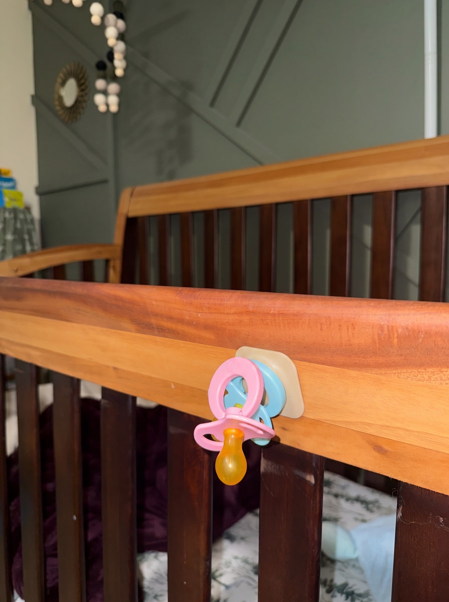 Sky and Blush Magnetot pacifiers attached together to a tan magnetic tile on a wooden crib rail