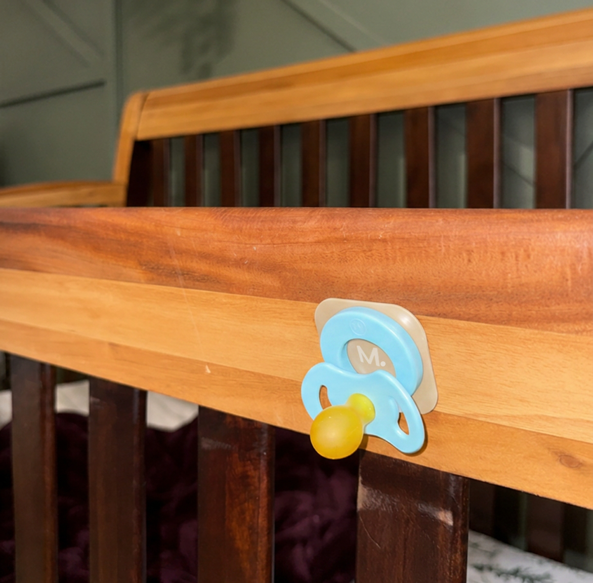 Sky Magnetot pacifier attached to the tan magnetic tile on a wooden crib rail